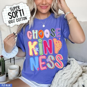 May include: A blue t-shirt with the words "CHOOSE KINDNESS" in colorful, bubble letters. The shirt also has a graphic that says "SUPER SOFT! 100% COTTON". The shirt is a comfortable, casual style.