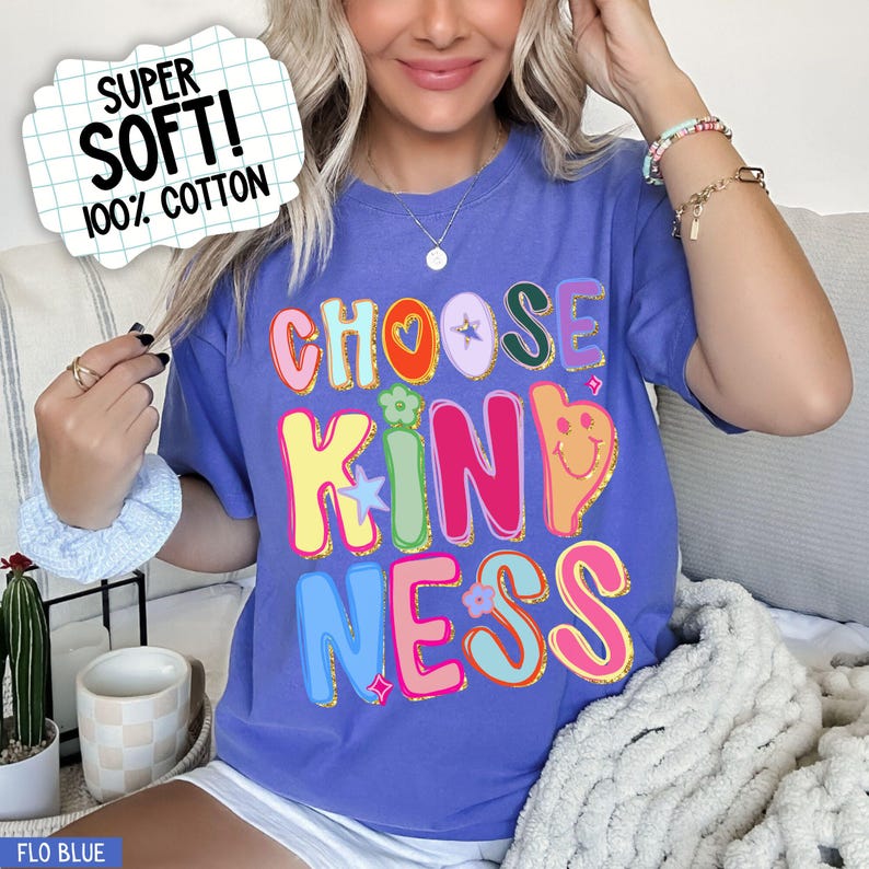 May include: A blue t-shirt with the words "CHOOSE KINDNESS" in colorful, bubble letters. The shirt also has a graphic that says "SUPER SOFT! 100% COTTON". The shirt is a comfortable, casual style.
