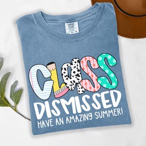 May include: A light blue t-shirt with the text "Class Dismissed Have an Amazing Summer!" in white. The word "Class" is in colorful letters with different patterns.