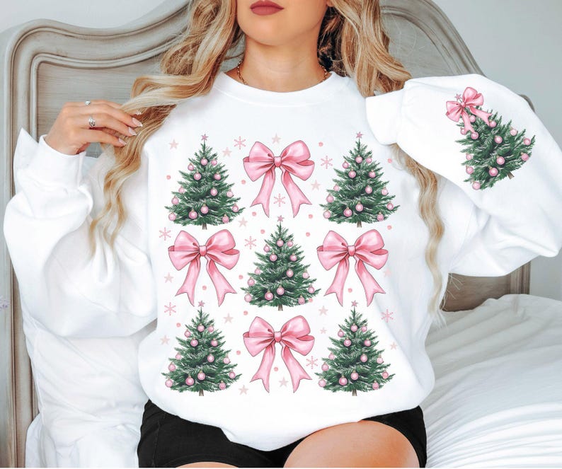 May include: White sweatshirt featuring a festive design with green Christmas trees adorned with pink ornaments and bows. The design is repeated across the front and on the sleeve, with snowflakes scattered around the trees and bows.