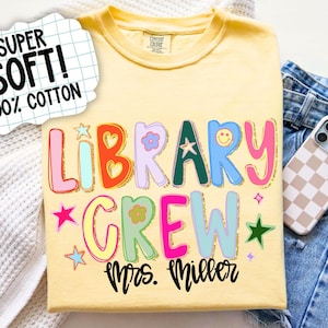 Może przedstawiać: Ż&oacute;łta koszulka z napisem "LIBRARY CREW Mrs. Miller" w kolorowych, zabawnych literach. Koszulka posiada r&oacute;wnież grafiki uśmiechniętych buziek i gwiazdek. Tekst "SUPER SOFT! 100% COTTON" znajduje się w białym dymku.