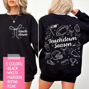 May include: Black sweatshirt with white text and graphics. The front says "touch down" with a bow graphic. The back features football-themed illustrations and the words "Touchdown Season". Available in five colors.