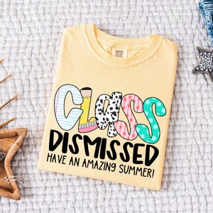 May include: A yellow t-shirt with the text "Class Dismissed Have an Amazing Summer!" in black lettering. The word "Class" is made up of colorful letters with different patterns.