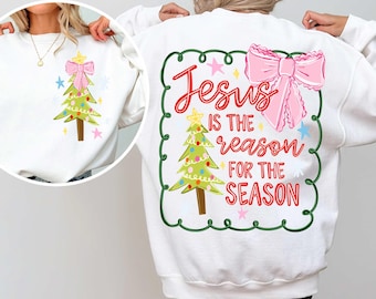 May include: White sweatshirt featuring a Christmas tree design with a pink bow and star accents. The back of the sweatshirt displays the text "Jesus is the reason for the season" in red script, framed by a green border and a pink bow.
