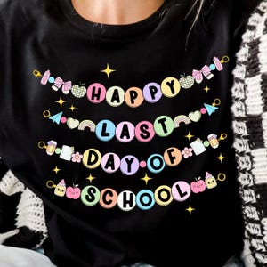 May include: Black t-shirt with a colorful banner that reads "Happy Last Day of School". The banner is made of small circles with different school-themed icons.