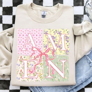 May include: A beige sweatshirt with a floral print design that spells out the word "AMEN".
