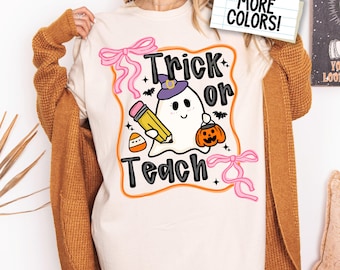 Puede incluir: Camiseta de manga larga color marfil con un diseño de Halloween. El diseño presenta un fantasma con un sombrero de bruja, sosteniendo un lápiz y una calabaza, con las palabras "Trick or Teach". Lazos rosas y estrellas rodean el diseño.