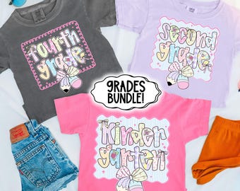 May include: Three short-sleeved t-shirts in gray, lavender, and pink, each with a grade level design. The designs include the words "Fourth Grade", "Second Grade", and "Kindergarten" in a colorful, playful font. The image also includes denim shorts and sunglasses.