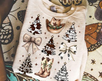May include: A beige sweatshirt featuring a festive design with Christmas trees, cowboy boots, bows, and a cowboy hat. The trees have brown and white cow print patterns. The hat has a star and holly. The bows have star accents.