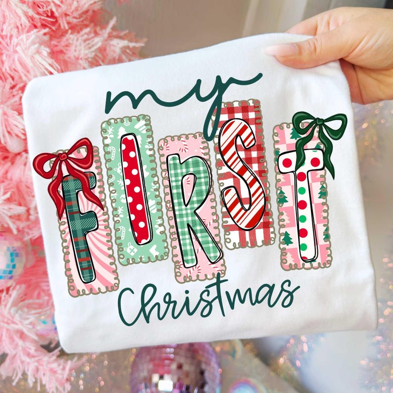 May include: White t-shirt with the text "my FIRST Christmas" in a festive design. The letters are decorated with patterns like polka dots, plaid, and candy canes, with bows on the "F" and "T".