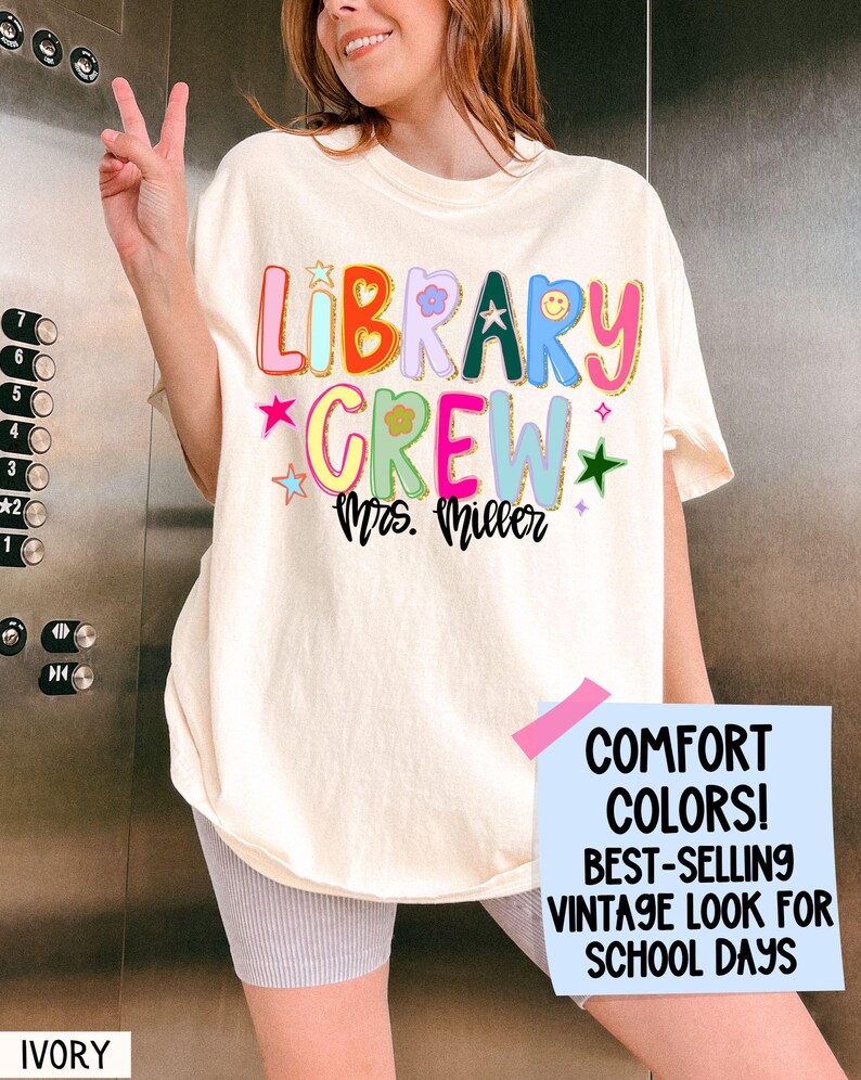 Może przedstawiać: Kremowa koszulka z napisem "LIBRARY CREW Mrs. Miller" w kolorowych, zabawnych literach. Koszulka posiada gwiazdki, kwiaty i uśmiechniętą buzię. Część kolekcji "COMFORT COLORS! BEST-SELLING VINTAGE LOOK FOR SCHOOL DAYS".