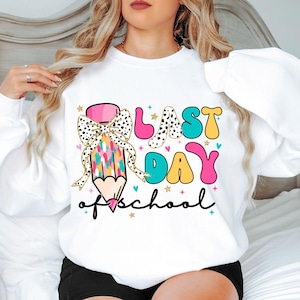 Op de afbeelding: Wit sweatshirt met een kleurrijke afbeelding van een potlood met een strik, de woorden "Laatste schooldag" en sterren.