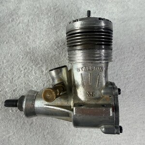 May include: A silver-toned metal Stallion 35 glow engine for remote-controlled vehicles. The engine features a cylindrical finned head, a threaded drive shaft, a brass-colored needle valve adjustment knob, and the text Stallion 35 embossed on the side.
