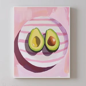 Könnte beinhalten: Zwei Hälften einer Avocado auf einem rosa-weiß gestreiften Teller. Die Avocadohälften befinden sich auf einem rosa Hintergrund.