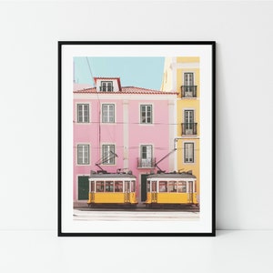 May include: Two yellow vintage streetcars parked in front of a pink and yellow building with a blue sky in the background.