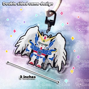 May include: Double-sided acrylic charm featuring a white and blue robot with wings. The robot is approximately 3 inches tall and has a detailed design. The charm is attached to a black metal keychain.