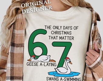 May include: Cream-colored sweatshirt with a Christmas-themed graphic. The design features the numbers 6 and 7 in green, with illustrations of geese and swans wearing Santa hats. Text reads "THE ONLY DAYS OF CHRISTMAS THAT MATTER".