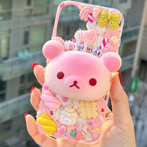 Op de afbeelding: Roze telefoonhoesje met een 3D-beerontwerp en de naam "EMMA". De hoes is versierd met roze glazuur, een gele strik, een wafel en een aardbei.
