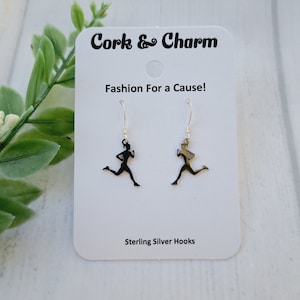 Puede incluir: Un par de pendientes de plata de ley con la silueta de una mujer corriendo. Los pendientes están en una tarjeta blanca con el texto "Cork & Charm" y "Fashion For a Cause!" La tarjeta también dice "Sterling Silver Hooks".