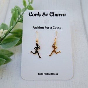 May include: Gold-plated earrings featuring a runner silhouette. The earrings are on a white card with the text "Cork & Charm Fashion For a Cause! Gold Plated Hooks".