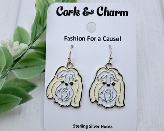 Puede incluir: Un par de pendientes de oro con un diseño de perro Shih Tzu blanco. Los pendientes están en una tarjeta blanca con el texto "Cork & Charm Fashion For a Cause! Sterling Silver Hooks".