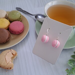 May include: Pink macaron shaped earrings with white accents on a white card. The earrings are hanging from silver hooks.
