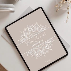Peut inclure: Une tablette numérique avec une couverture beige ornée d'un motif mandala blanc et du texte "Mon Journal Renaissance". La tablette est posée sur une surface blanche, avec un casque argenté et un petit vase avec des fleurs séchées en arrière-plan.