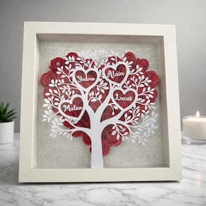 Puede incluir: Obra de arte en papel enmarcada, con un diseño de árbol blanco y una corona en forma de corazón llena de rosas de papel rojas. Los nombres Yadira, Alain, Lucas y Mateo están presentes. El marco es blanco.