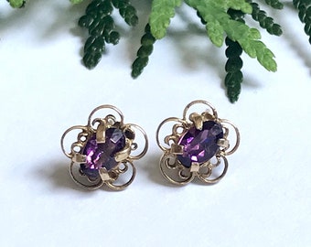 May include: A pair of gold earrings with a delicate floral design and oval-shaped purple gemstones.