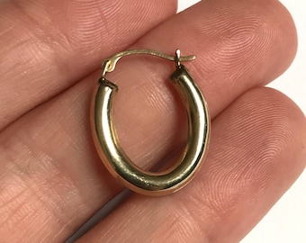 May include: A small, oval-shaped gold hoop earring with a polished, reflective surface. The earring features a hinged post mechanism at the top, allowing it to open and close securely. The design is simple, smooth, and circular in its overall form.