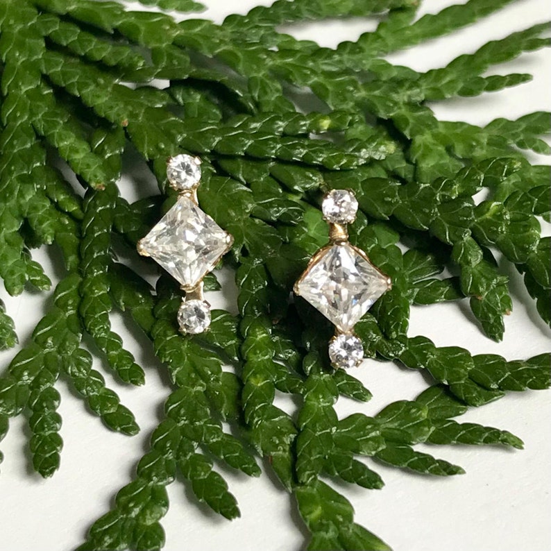 May include: A pair of gold earrings with a square-shaped diamond in the centre and two smaller diamonds on either side.