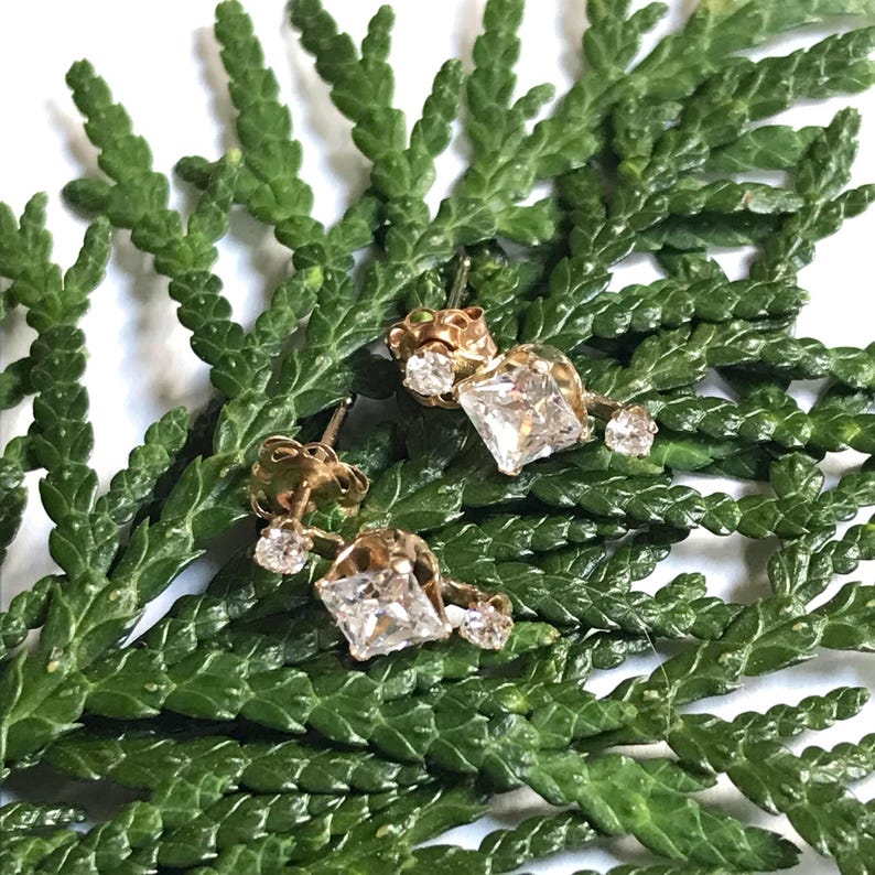 May include: A pair of gold earrings with a square-shaped diamond in the centre and smaller diamonds surrounding it.