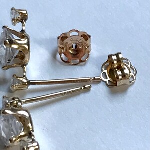 May include: A pair of gold earrings with a small diamond in each setting. The earrings have a post back and a small, decorative piece on the back of the post.