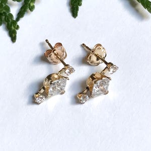 May include: A pair of gold earrings with a square-shaped diamond in the centre and two smaller diamonds on each side.