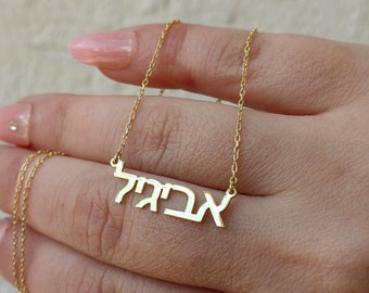 May include: A gold chain necklace with a nameplate pendant that reads "אביגיל" in Hebrew.