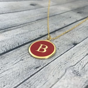 May include: A gold chain necklace with a red circular pendant featuring a gold letter "B" in the centre.