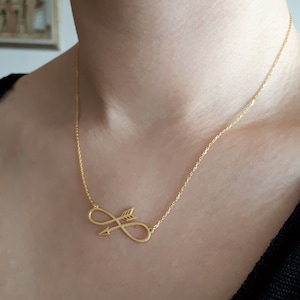 May include: A gold necklace with an infinity symbol pendant and an arrow going through it.