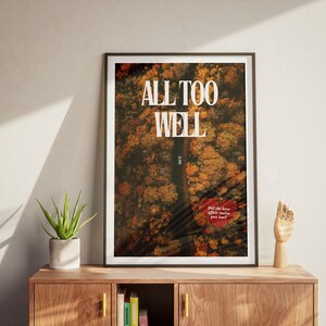 May include: A framed poster with an aerial photograph of a road through a forest in autumn colors. The text "ALL TOO WELL" is printed in white on the poster. The text "Did the love affair make you famous?" is printed in red on the poster.