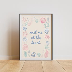 May include: A framed print with a cream background and a blue and pink illustration of seashells, starfish, and seaweed. The text "Meet me at the beach" is written in blue cursive.