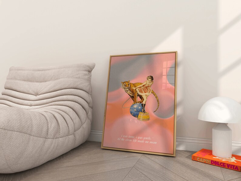 May include: A framed print with a pink and blue background featuring a woman in a red and white costume riding a tiger on a ball. The text below reads "I can tame, I was gentle, all the circus life made me mean."