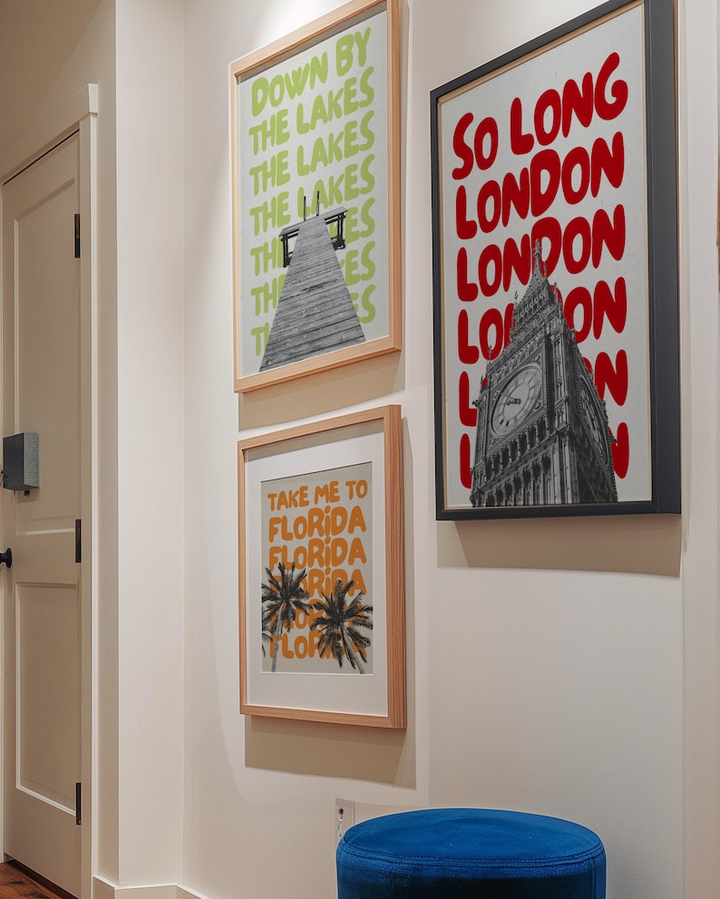 May include: Three framed art prints on a white wall. The print on the left has a green background with the text "Down by the Lakes" repeated in a stacked pattern. The print in the middle has a beige background with the text "Take me to Florida" repeated in a stacked pattern. The print on the right has a black frame and a black and white photo of Big Ben with the text "So Long London" repeated in a stacked pattern in red.