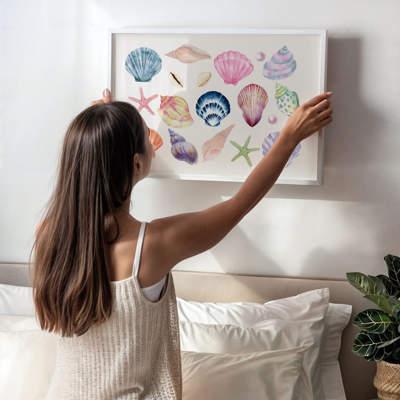 May include: A framed watercolor painting of various seashells in shades of pink, blue, purple, and green. The shells are arranged in a random pattern on a white background.
