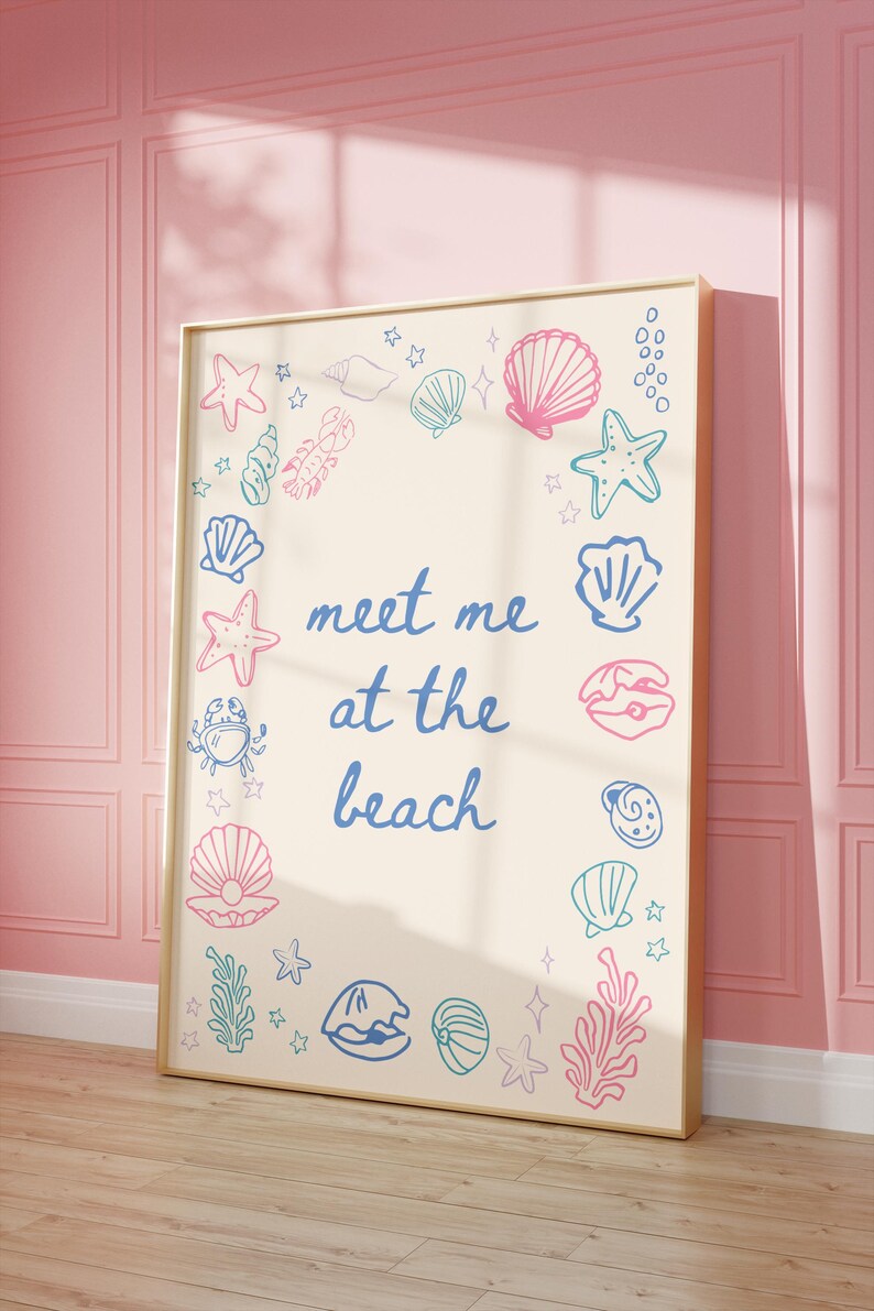 May include: A beige poster with a gold frame features a blue and pink illustration of seashells, starfish, and seaweed. The text "meet me at the beach" is written in blue cursive.