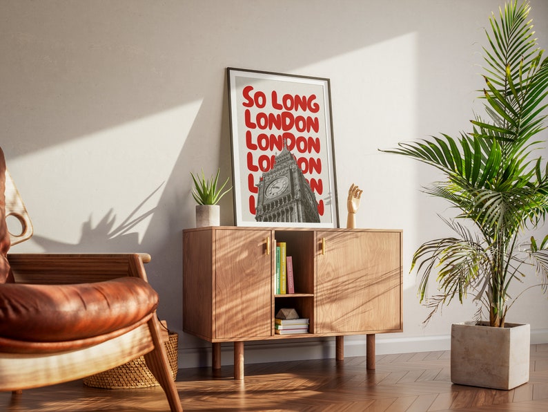 May include: A framed print with a black frame and a white background. The print features a photo of Big Ben in London with the text "So Long London" repeated in red letters.