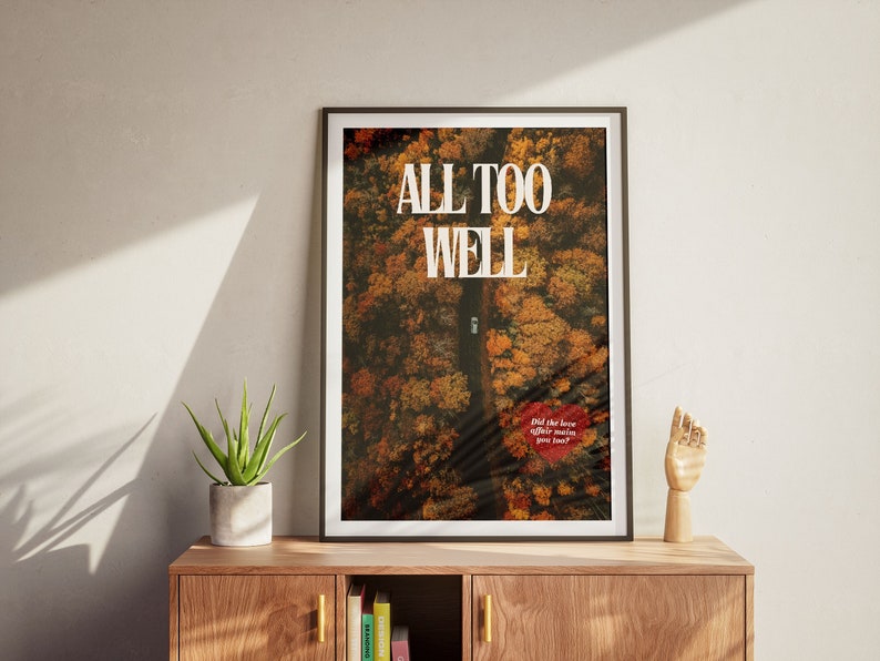May include: A framed poster with an aerial photograph of a road through a forest in autumn colors. The text "ALL TOO WELL" is printed in white on the poster. The text "Did the love affair make you famous?" is printed in red on the poster.