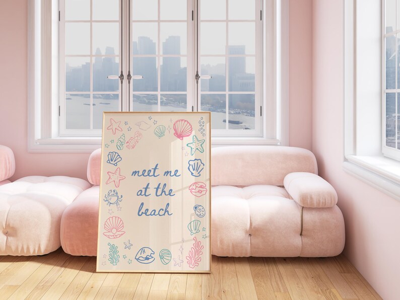 May include: A framed print with a light beige background and a blue inscription that reads "meet me at the beach". The inscription is surrounded by a border of colourful illustrations of seashells, starfish, and seaweed.