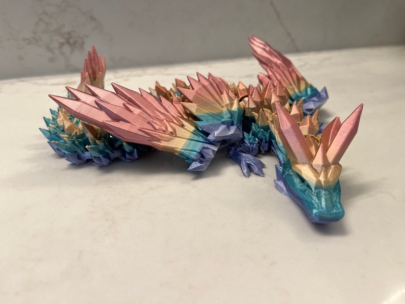 May include: A multi-colored, crystal-like dragon figurine with a rainbow gradient. The dragon is made of plastic and has a detailed, textured surface.