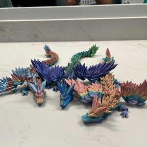 May include: Four origami dragons made of paper, each with a different color scheme. The dragons are arranged in a group, with their wings spread out. The dragons are made of paper and have a shiny, iridescent finish.