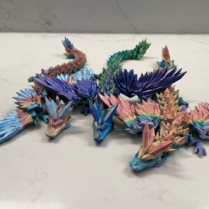 May include: Five origami dragons made of paper, each with a different color gradient. The dragons are arranged in a circle, with their heads facing inwards. The colors of the dragons are blue, purple, green, pink, and orange.