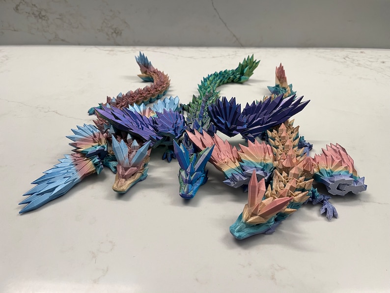 May include: Five origami dragons made of paper, each with a different color gradient. The dragons are arranged in a circle, with their heads facing inwards. The colors of the dragons are blue, purple, green, pink, and orange.